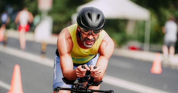 Smiling man in sportswear and helmet competing on bicycle riding on asphalt road