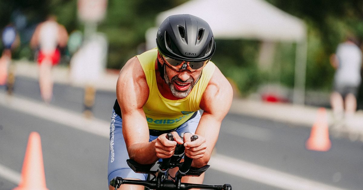 Smiling man in sportswear and helmet competing on bicycle riding on asphalt road
