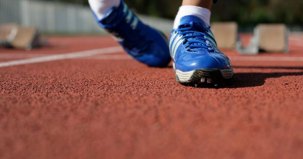 Close-up of a runner's blue shoes on a track, ready to race outdoors.