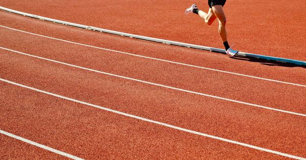 Athlete running on a red track in an outdoor stadium on a sunny day.