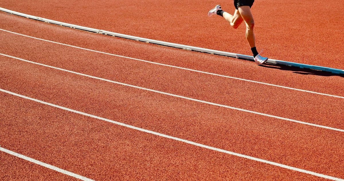 Athlete running on a red track in an outdoor stadium on a sunny day.