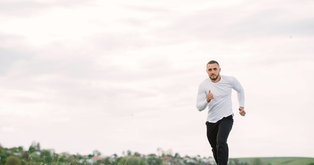 Adult man running on an empty road in casual sportswear, showcasing fitness and healthy lifestyle.