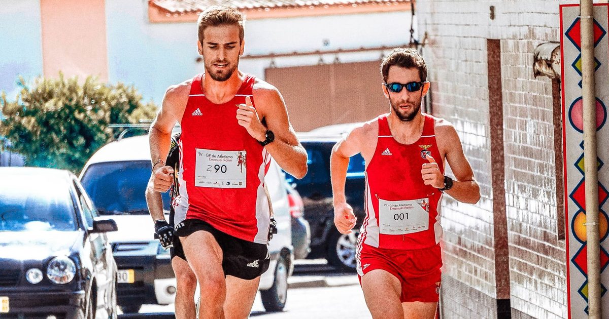 Two men in red outfits running in an urban marathon during the day.