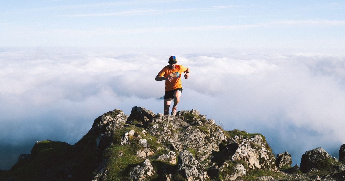 Man running on rocky mountain peak above the clouds, symbolizing achievement and adventure.
