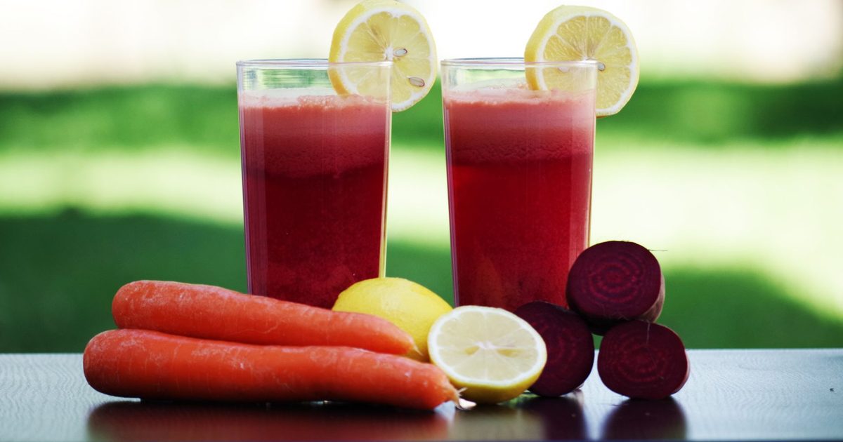 Colorful glasses of beetroot and carrot juice garnished with lemon slices, symbolizing health and freshness.