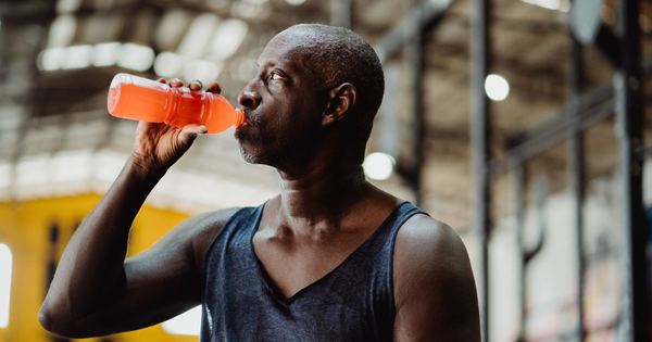 An athletic man enjoys a refreshing energy drink during his workout in a gym setting.