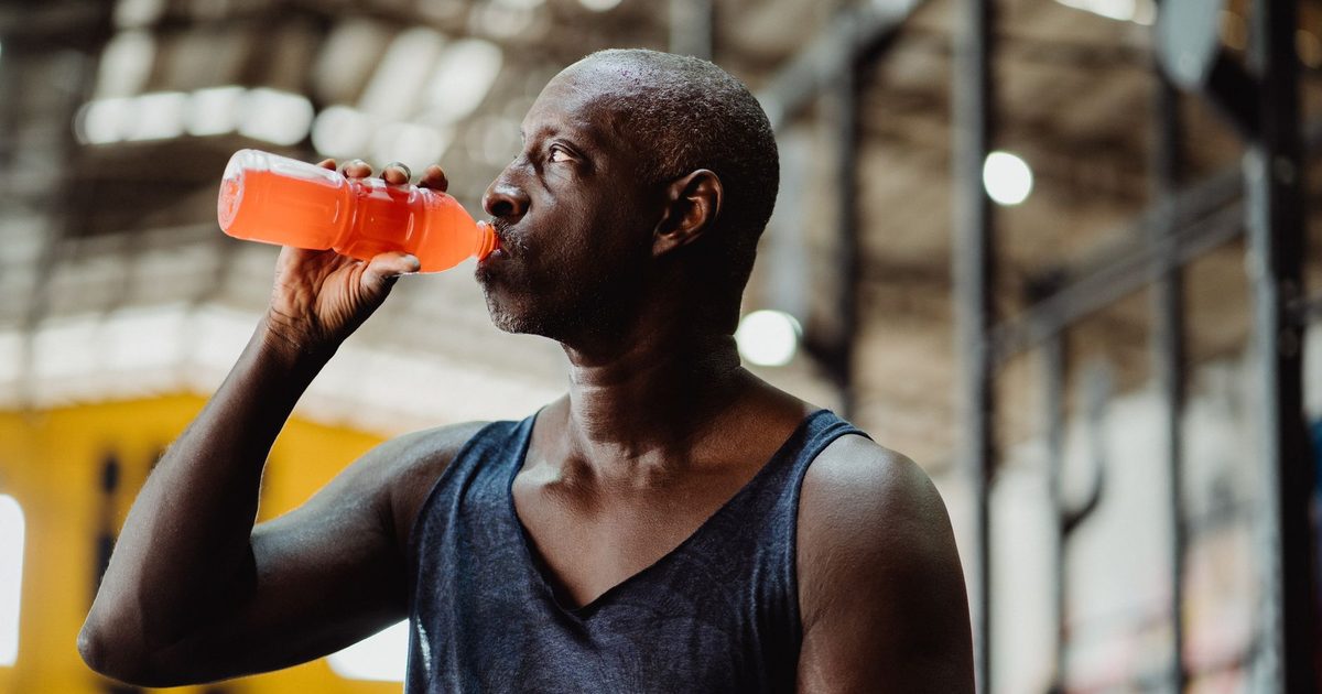 An athletic man enjoys a refreshing energy drink during his workout in a gym setting.