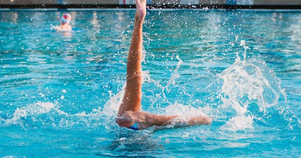 Dynamic shot of a synchronized swimmer performing an artistic leg move in a pool.