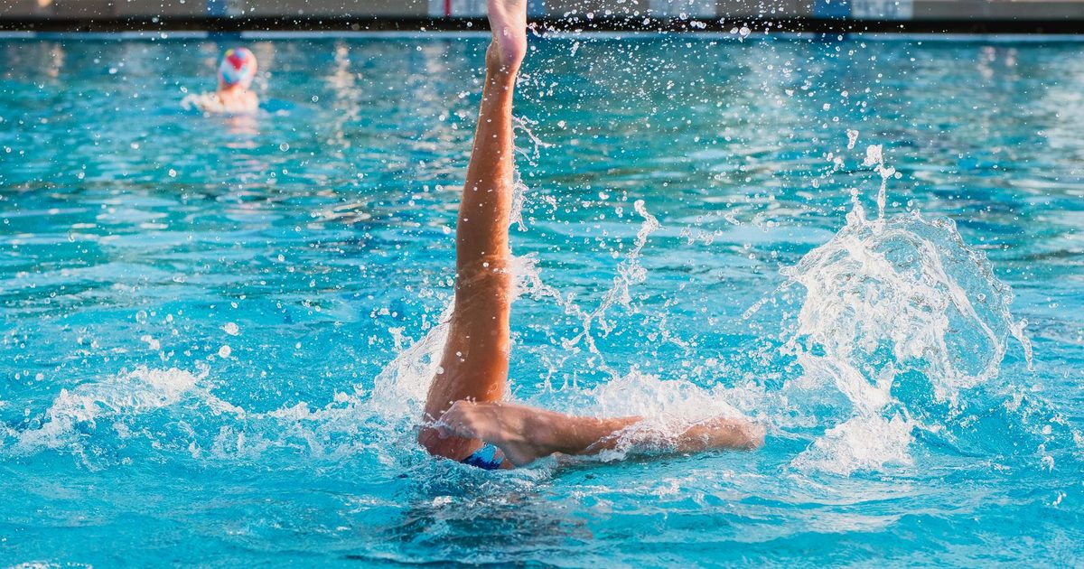 Dynamic shot of a synchronized swimmer performing an artistic leg move in a pool.