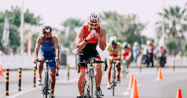 Fit male bicyclist drinking beverage while riding bicycle behind unrecognizable rivals during race on roadway in city