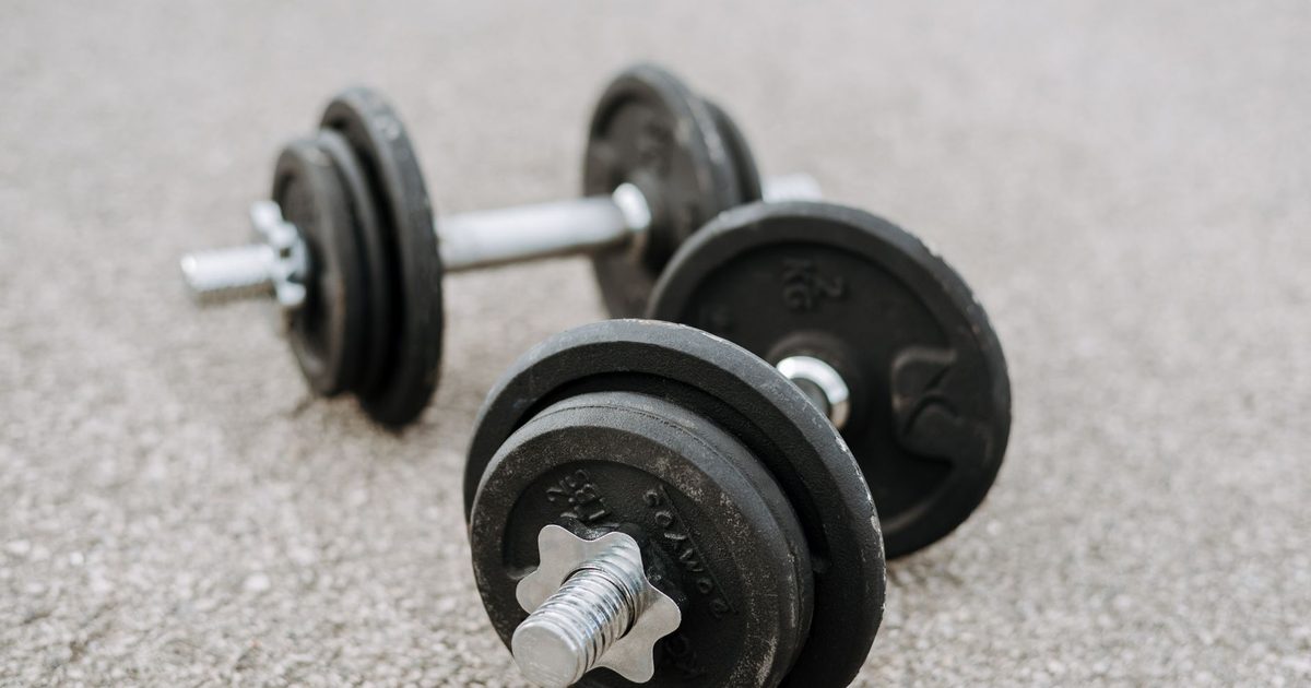 Massive metal dumbbells prepared for difficult healthy training on asphalt road in summer