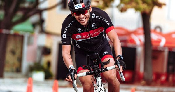 Smiling cyclist in helmet racing on road bike during a sunny day.