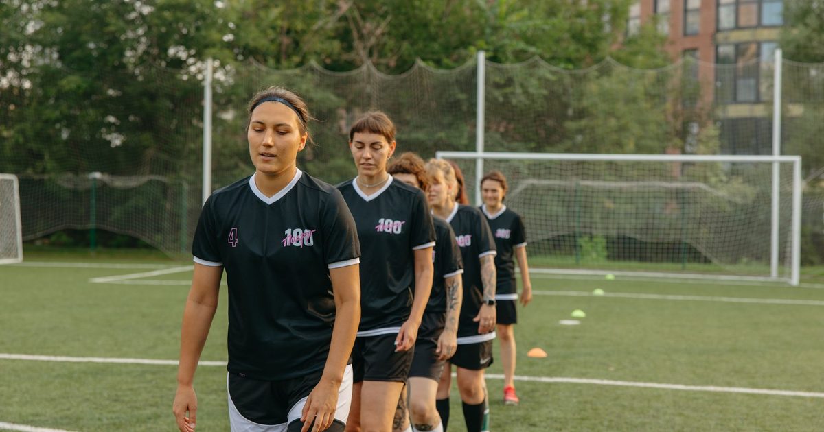 Women soccer players training on a green football field during the day.