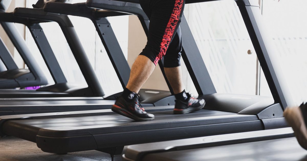 A person walking on a treadmill in a modern gym setting, focusing on fitness.