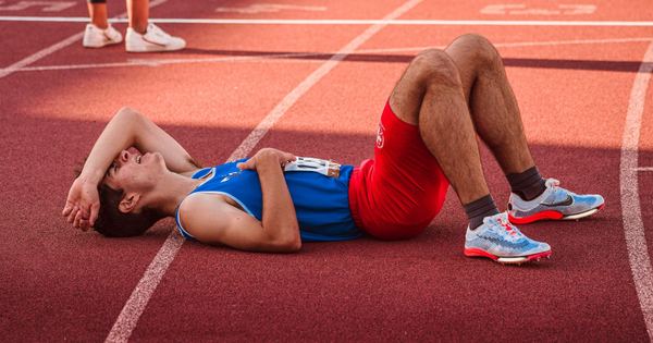 A tired athlete lies on the track, recovering after a race in sportswear.