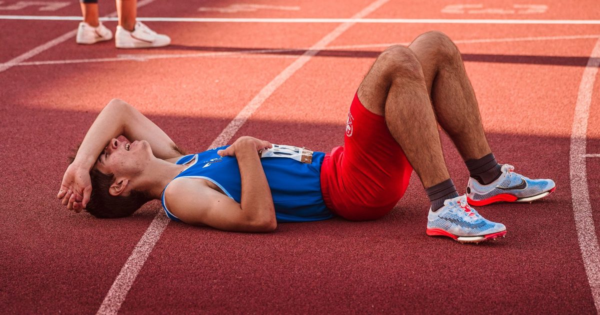 A tired athlete lies on the track, recovering after a race in sportswear.