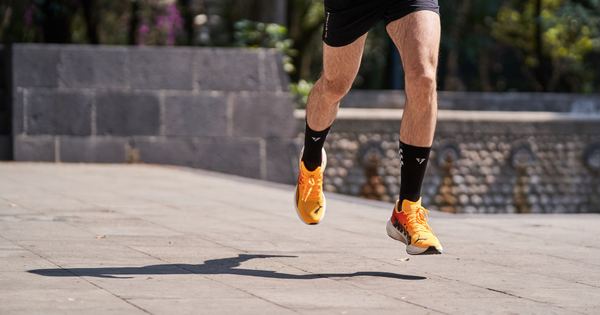 Male runner with orange shoes sprinting outdoors on a sunny day, showing athleticism.