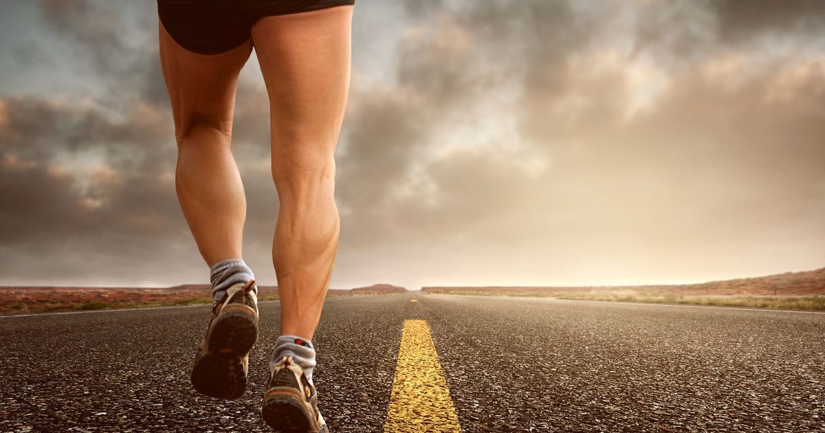 Runner's legs on a road during a sunset, symbolizing endurance and outdoor fitness training.