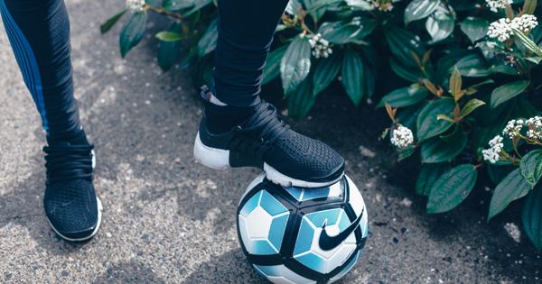 Athlete in black sportswear controls a soccer ball near greenery outdoors.