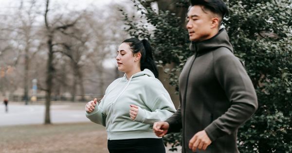 Side view of overweight woman in sportswear running with Asian trainer in city park in daytime