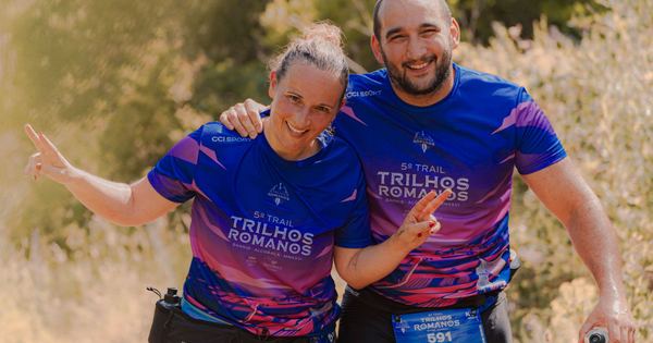Two adult marathon runners in bright purple jerseys pose happily during an outdoor trail race.