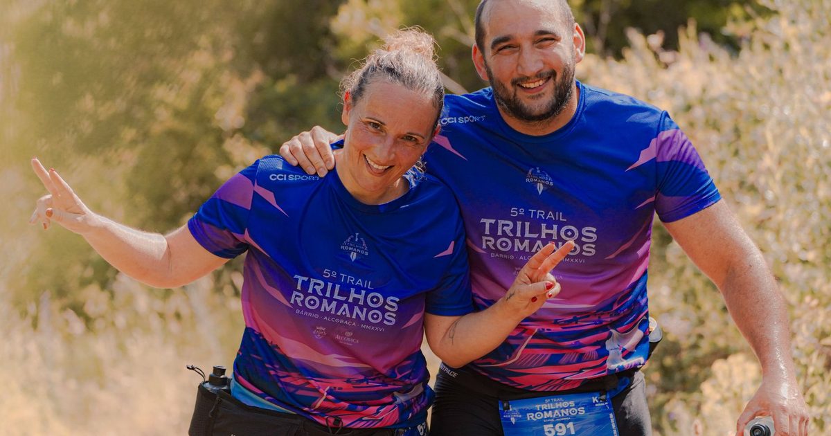Two adult marathon runners in bright purple jerseys pose happily during an outdoor trail race.