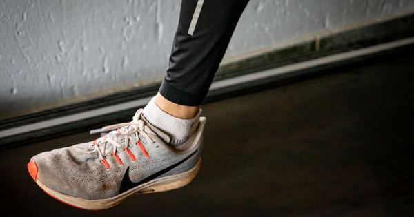 A detailed view of a sneaker mid-stride on a treadmill, showcasing active lifestyle footwear.