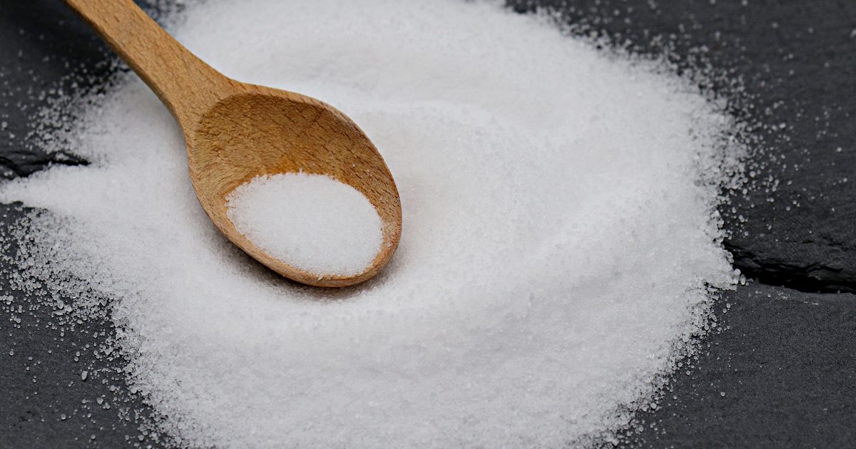Close-up of a wooden spoon with sea salt on a slate background, perfect for culinary themes.