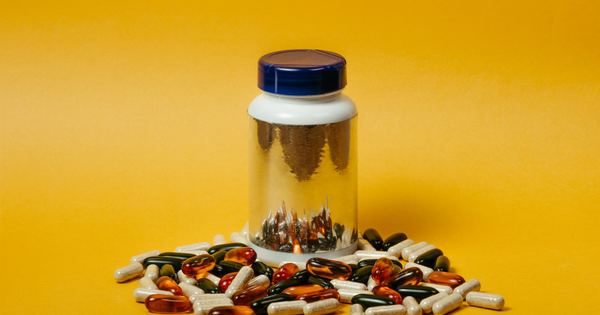 Vibrant collection of multi-colored pills and capsules surrounding a reflective pill bottle on a bright yellow background.