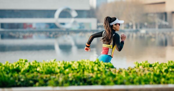 Woman running along an urban lakeside path, exercising with focus and determination amidst cityscape.