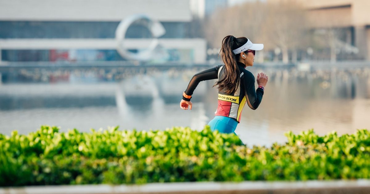Woman running along an urban lakeside path, exercising with focus and determination amidst cityscape.