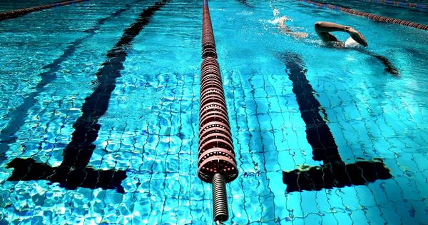 A person swimming in a clear blue outdoor pool with lane dividers.