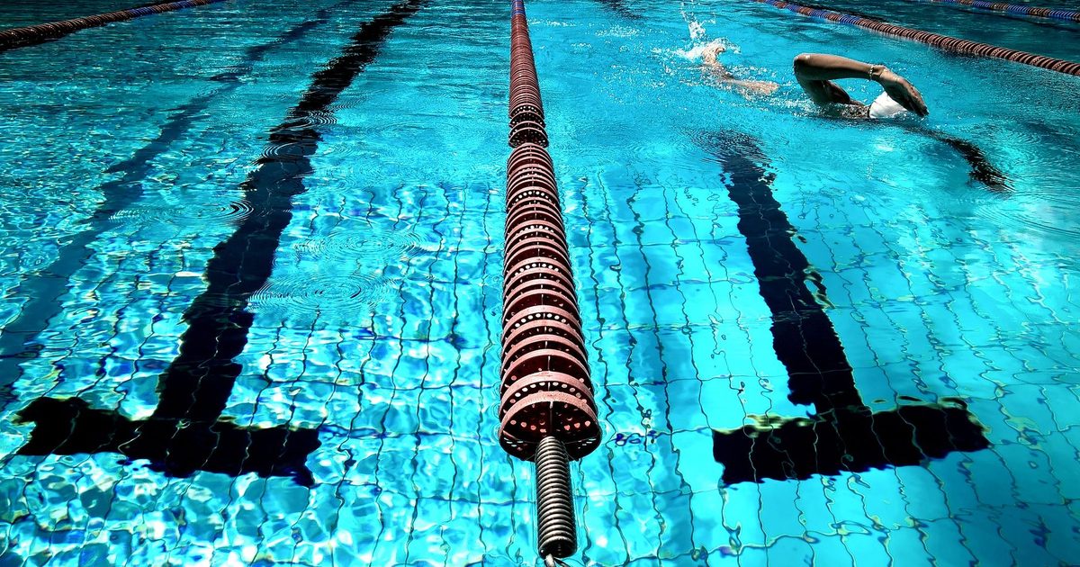 A person swimming in a clear blue outdoor pool with lane dividers.