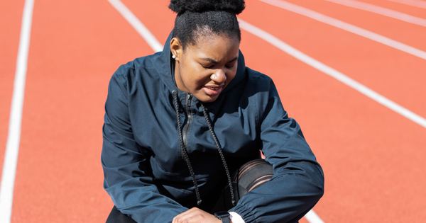A woman in activewear on a running track checks her smartwatch after a workout.